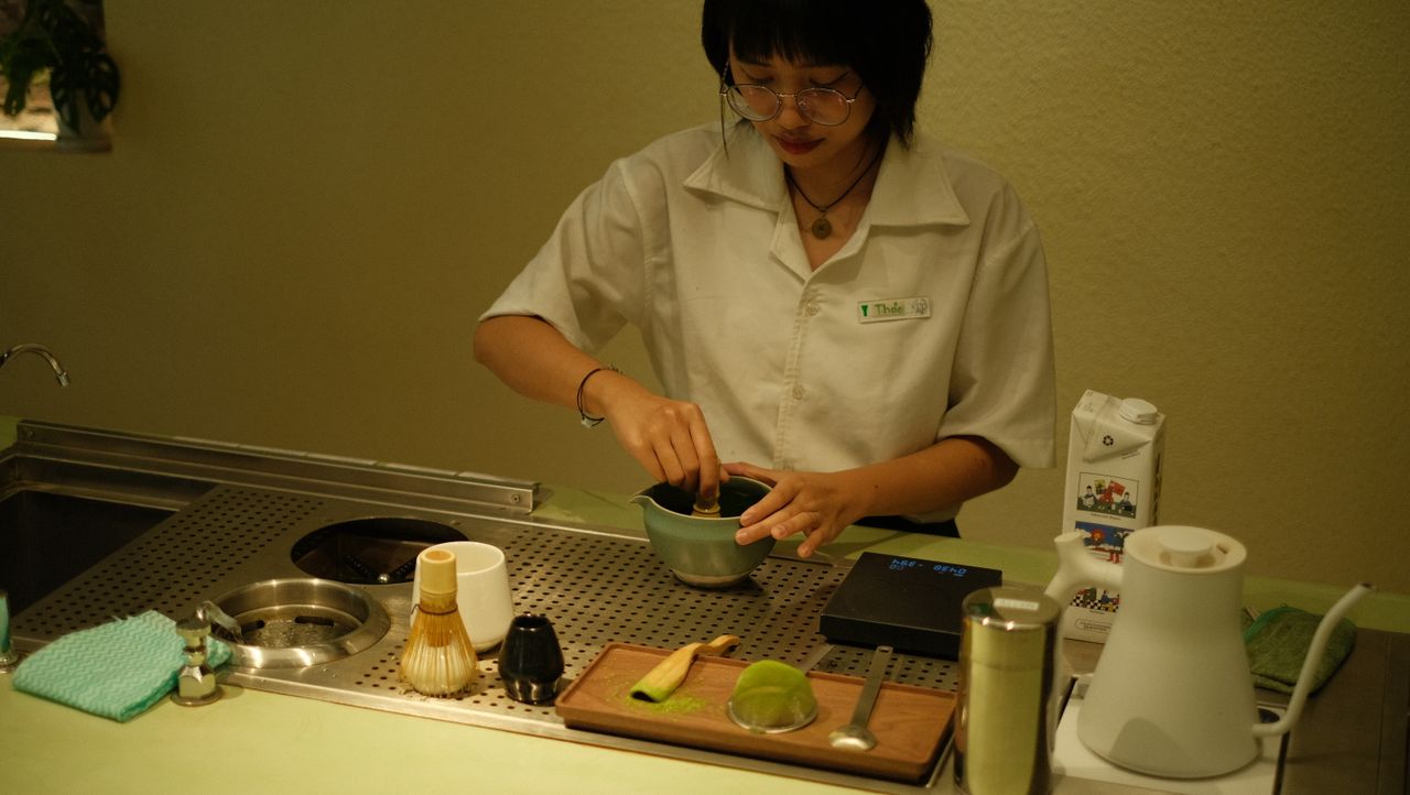 A barista mixing matcha tea in a contemporary tea setting, creating an inviting atmosphere.