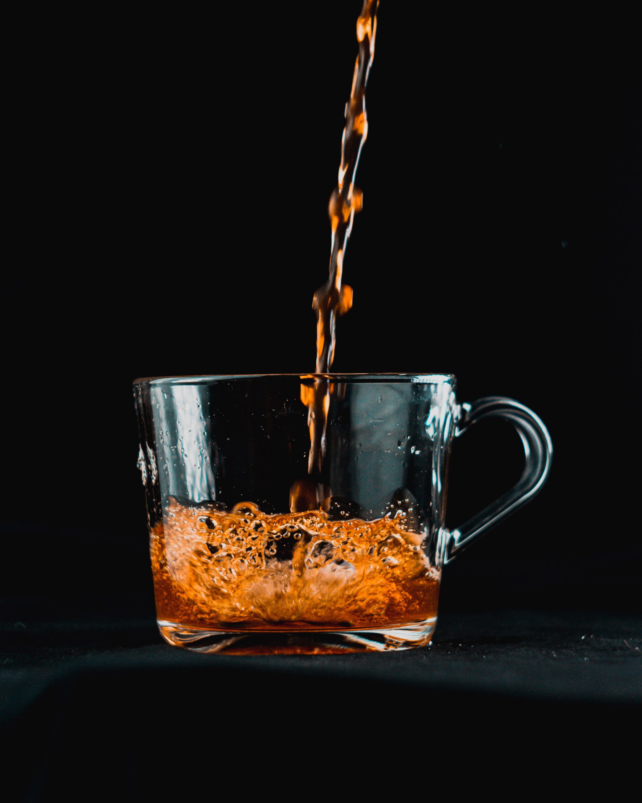 Close-up of amber liquid being poured into a clear glass mug against a black background.